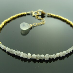 May include: A gold and white bracelet with a delicate chain and a small, clear gemstone pendant. The bracelet is made of small, faceted beads of gold and white rough diamonds.