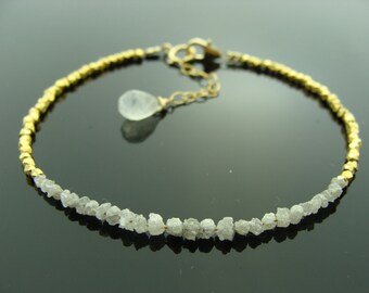 May include: A gold and white bracelet with a delicate chain and a small, clear gemstone pendant. The bracelet is made of small, faceted beads of gold and white rough diamonds.