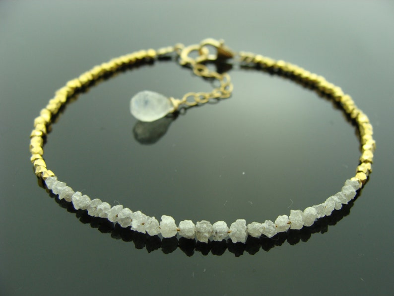May include: A gold and white bracelet with a delicate chain and a small, clear gemstone pendant. The bracelet is made of small, faceted beads of gold and white rough diamonds.
