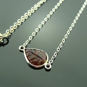 Puede incluir: Un collar de cadena de plata con un colgante en forma de l&aacute;grima con una piedra preciosa roja.