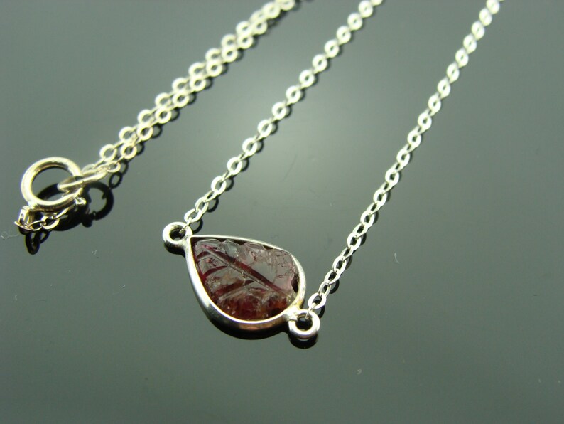 Puede incluir: Un collar de cadena de plata con un colgante en forma de l&aacute;grima con una piedra preciosa roja.