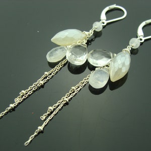May include: Silver dangle earrings with multiple clear and white gemstone drops. The earrings have a chain design with small silver beads.