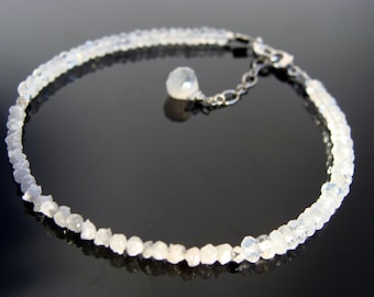 Puede incluir: Un delicado brazalete de cadena de plata con un pequeño colgante de piedra preciosa redonda blanca. El brazalete está hecho de pequeñas piedras preciosas blancas facetadas.