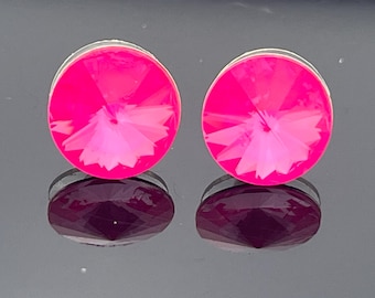 Puede incluir: Par de pendientes de botón redondos de color rosa brillante con un diseño facetado similar al cristal. Los pendientes están engarzados en un metal plateado y reflejan la luz, creando un efecto brillante. Los pendientes se muestran sobre una superficie reflectante.