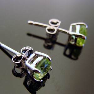 May include: A pair of silver stud earrings with green gemstones. The earrings have a post and butterfly back.