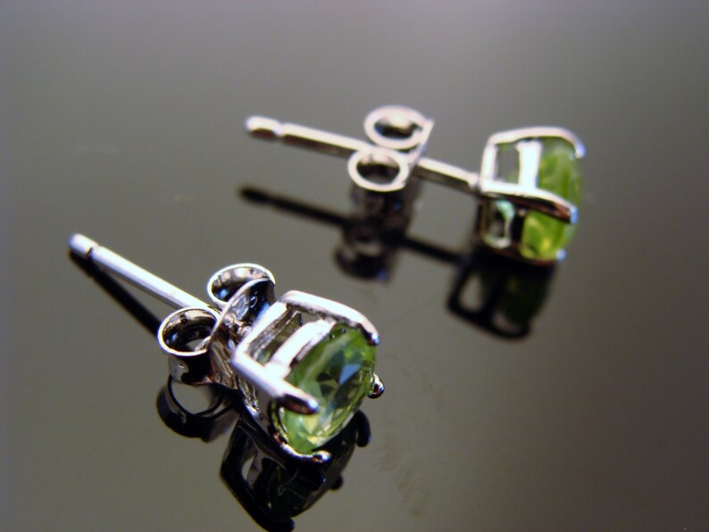 May include: A pair of silver stud earrings with green gemstones. The earrings have a post and butterfly back.