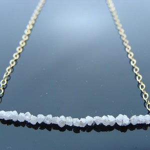 May include: A delicate gold chain necklace with a row of small, white rough diamonds.