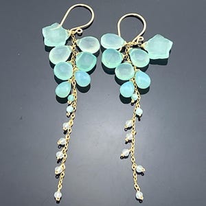 May include: A pair of elegant dangle earrings featuring a cluster of light blue gemstones and small white beads suspended from gold-colored hooks. The earrings have a delicate, cascading design, perfect for adding a touch of sophistication.