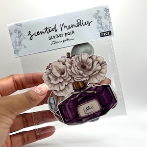 Puede incluir: Un paquete de pegatinas "Scented Memories" con un diseño de frasco de perfume y detalles florales. Las pegatinas están en un paquete de plástico transparente, con el texto "7 PCS" visible. El frasco de perfume es de color púrpura oscuro.