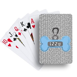 May include: A deck of playing cards with a custom dog bone design. The cards fanned out show the 10 of hearts, Jack of clubs, Queen of diamonds, King of clubs, and Ace of hearts. The back of the deck has a blue dog bone with the name "Izzy".