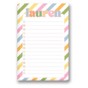 Peut inclure: Bloc-notes personnalisé avec le nom "Lauren" en lettres colorées. L'intérieur est ligné pour l'écriture et bordé de rayures aux couleurs pastel : rose, bleu, jaune et vert. Parfait pour les listes et les notes.