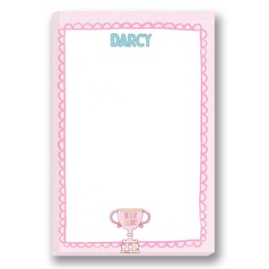 May include: A pink notepad with a scalloped border and the name "DARCY" in blue letters at the top. A trophy with the words "BEST AUNT" is at the bottom. The notepad is designed with a light pink background.