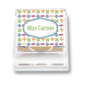 May include: A clear acrylic sticky note holder with a patterned top featuring colorful math symbols. The label in the center reads "Miss Carmen" in green text, perfect for a teacher's desk or office. The holder is designed to dispense sticky notes.
