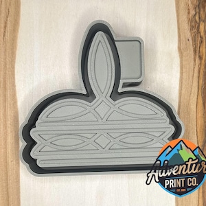 Puede incluir: Un cortador de galletas de plástico gris y negro con forma de conejito con un patrón decorativo. El cortador de galletas está sobre una superficie de madera clara. El logotipo de Adventure Print Co. está en la esquina inferior derecha.