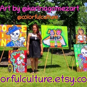 May include: A woman stands in front of a display of colorful paintings on easels. The paintings feature Day of the Dead imagery, including skeletons and flowers. The text "Art by @karinagomezart @colorfulculture" is at the top of the image. The text "colorfulculture.etsy.com" is at the bottom of the image.