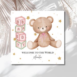 Puede incluir: Tarjeta de anuncio de nacimiento con una ilustración de acuarela de un oso de peluche con un lazo rosa, rodeado de estrellas doradas. La tarjeta incluye bloques de bebé que deletrean "BABY" y el texto "WELCOME TO THE WORLD" con un nombre debajo.