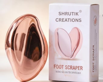 May include: A rose gold foot scraper with a smooth, curved design, next to a white box with the text "SHRUTIK CREATIONS FOOT SCRAPER NANO GLASS TECHNOLOGY". The scraper has a shiny, reflective surface.