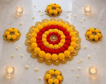 Puede incluir: Un arreglo floral circular con anillos concéntricos de flores de caléndula amarillas y rojas y un emblema dorado central. Cuatro coronas de caléndula más pequeñas a juego rodean el centro, junto con cuatro portavelas de cristal para té.