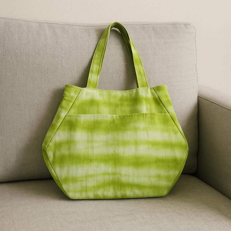 May include: A lime green tote bag with a horizontal tie-dye pattern. The bag features a hexagonal shape with a wide base, two matching fabric handles, and a large exterior slip pocket across the front panel, constructed from soft textile.