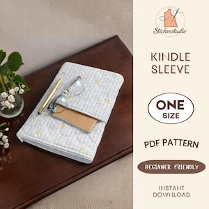 Puede incluir: Una funda Kindle acolchada azul claro y blanca con detalles de estrellas amarillas. La funda está abierta, revelando un cuaderno marrón y gafas. Un bolígrafo dorado descansa encima. El texto "Kindle Sleeve" y "One Size" son visibles.