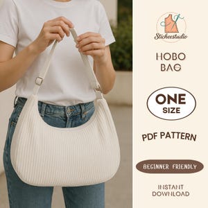 May include: Cream-colored hobo bag with a corduroy texture, held by a person wearing a white t-shirt and blue jeans. The bag has a long, adjustable strap and a silver-colored buckle. The text on the image says "Hobo Bag", "One Size", "PDF Pattern", "Beginner Friendly", and "Instant Download".