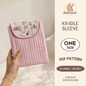May include: A quilted pink Kindle sleeve featuring a floral patterned flap with a small black snap button closure. The text on the right side reads Sticheestudio, KINDLE SLEEVE, ONE SIZE, PDF PATTERN, BEGINNER FRIENDLY, and INSTANT DOWNLOAD.