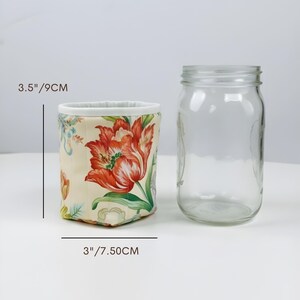 May include: A floral fabric container, 3.5 inches (9 cm) tall and 3 inches (7.50 cm) wide, with a cream background and red tulip design. Next to it is a clear glass jar.