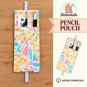 May include: A fabric pencil pouch featuring a white background with a colorful pattern of yellow, orange, and teal teardrop shapes. The pouch includes a white elastic strap and contains several pens and a clear plastic ruler inside the pocket.