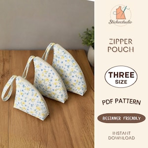 Op de afbeelding: Drie driehoekige ritszakjes met een witte achtergrond en een bloemenpatroon van kleine blauwe en gele bloemetjes. Elk zakje heeft een stoffen polsbandje. De tekst rechts luidt Sticheestudio ZIPPER POUCH THREE SIZE PDF PATTERN BEGINNER FRIENDLY INSTANT DOWNLOAD.