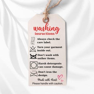 a white tag with instructions for washing clothes, including checking the care label, turning the garment inside out, avoiding harsh detergents, and not ironing the design.