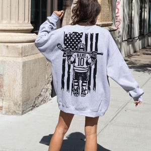 A person wearing a grey sweatshirt with a graphic design on the back, standing on a sidewalk.