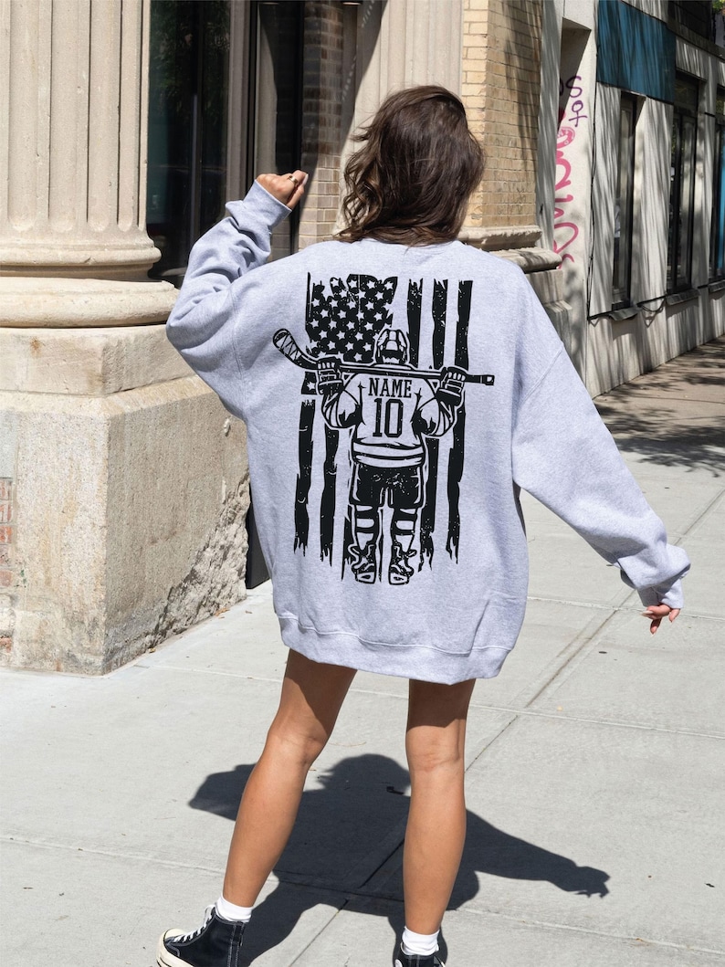 A person wearing a grey sweatshirt with a graphic design on the back, standing on a sidewalk.