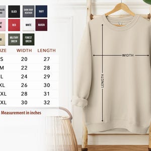 a beige sweater hanging on a wooden hanger, with a size chart and measurements provided below it.