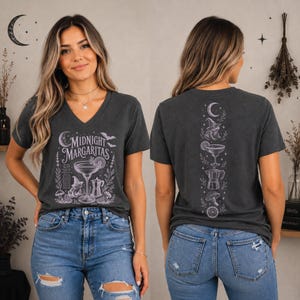 May include: A dark gray V-neck t-shirt featuring a white graphic print. The front displays a margarita glass, a witch hat, a coffee pot, and the text "MIDNIGHT MARGARITAS." The back shows a vertical design of a crescent moon, witch hat, and drink.