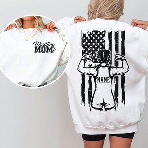 A person wearing a white sweatshirt with a black graphic design on the back, featuring a muscular figure and an American flag.