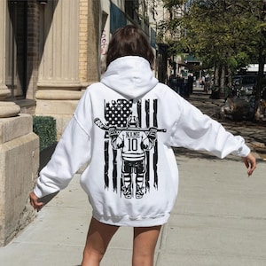A person wearing a white hoodie with a graphic design on the back is walking on a sidewalk.