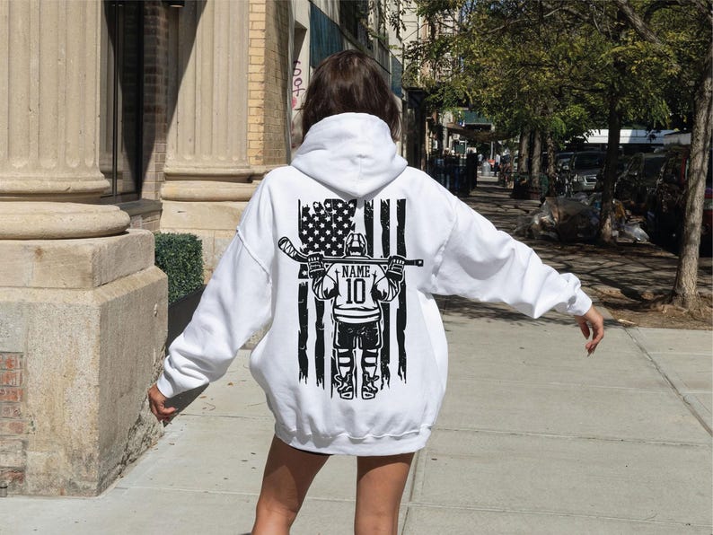 A person wearing a white hoodie with a graphic design on the back is walking on a sidewalk.