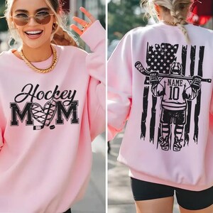 A woman wearing a pink sweatshirt with a graphic design on the back, including an American flag and a hockey player.