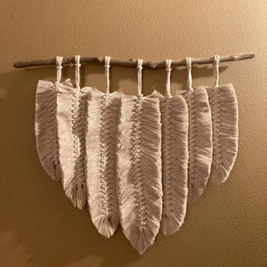 Colgante de pared con plumas de macramé color crema sobre madera de abedul