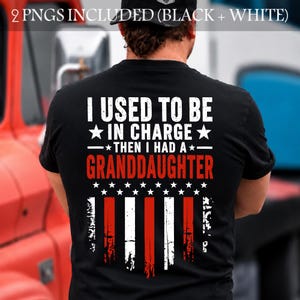 May include: Black t-shirt with the text "I USED TO BE IN CHARGE - THEN I HAD A - GRANDDAUGHTER" in white and red. The design includes a distressed American flag graphic.