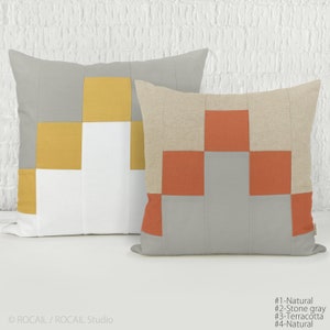 Peut inclure: Deux coussins carrés présentant un motif géométrique en patchwork. Le coussin de gauche affiche des blocs de tissu gris, jaune moutarde et blanc. Le coussin de droite présente des blocs de tissu terracotta, gris pierre et beige naturel.