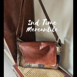 May include: A brown leather messenger bag with a flap closure. The bag has a patchwork design with various fabric textures and colors. The text "2nd Time Mercantile" is written on the bag.
