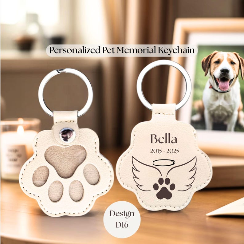 May include: Personalized pet memorial keychain in the shape of a paw. One keychain shows a paw print, the other has the name "Bella", dates, angel wings, and a paw print. The text "Personalized Pet Memorial Keychain" and "Design D16" are also visible.
