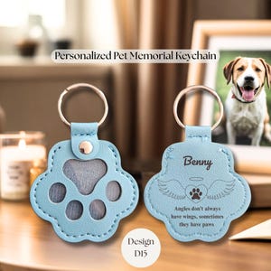 May include: Light blue paw-shaped keychain with a silver keyring. The keychain has a photo insert and the text "Benny" with angel wings and a paw print. The text "Angles don't always have wings, sometimes they have paws" is also visible. Design D15.