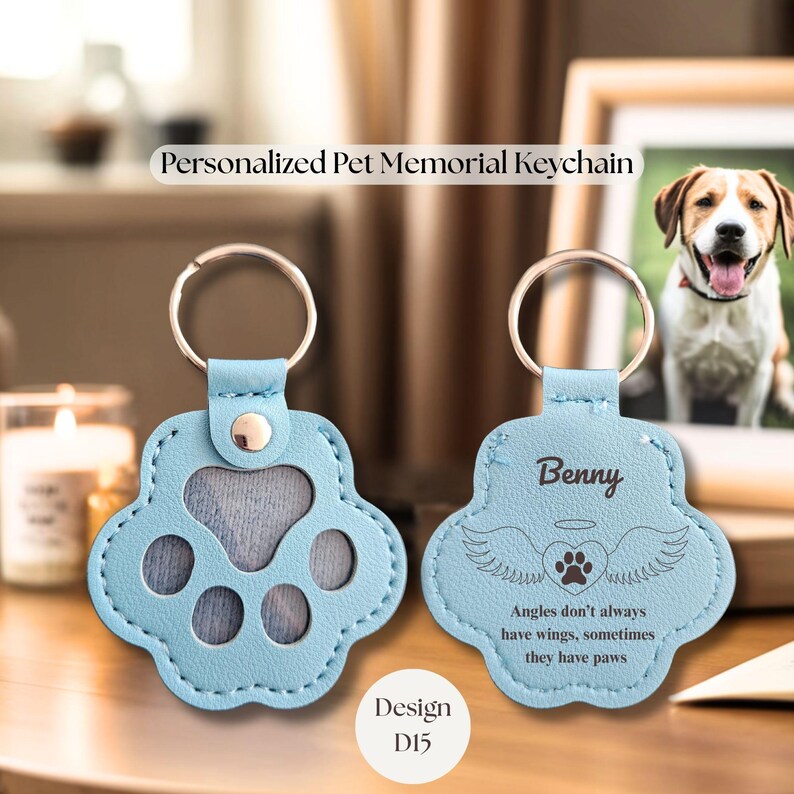 May include: Light blue paw-shaped keychain with a silver keyring. The keychain has a photo insert and the text "Benny" with angel wings and a paw print. The text "Angles don't always have wings, sometimes they have paws" is also visible. Design D15.