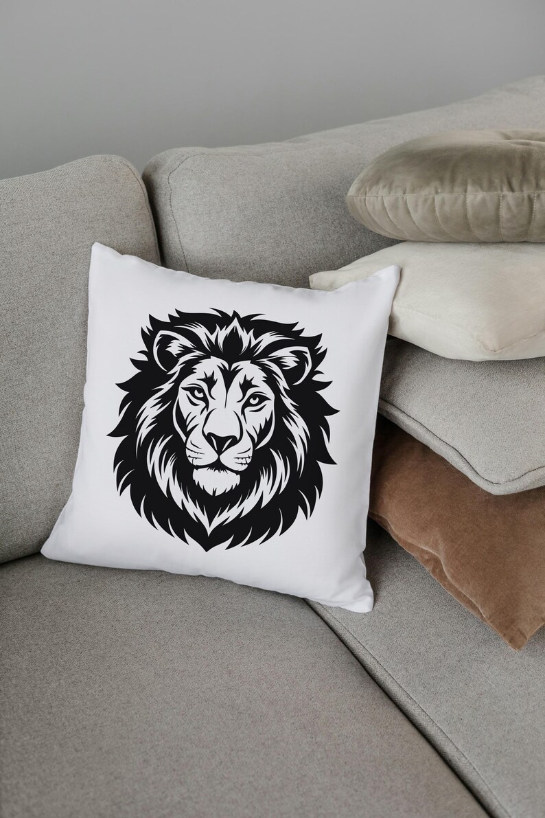 May include: White square throw pillow featuring a detailed black illustration of a lion's head. The lion's mane is prominently displayed, with intricate lines and shading. The pillow is placed on a gray sofa with other pillows in the background.