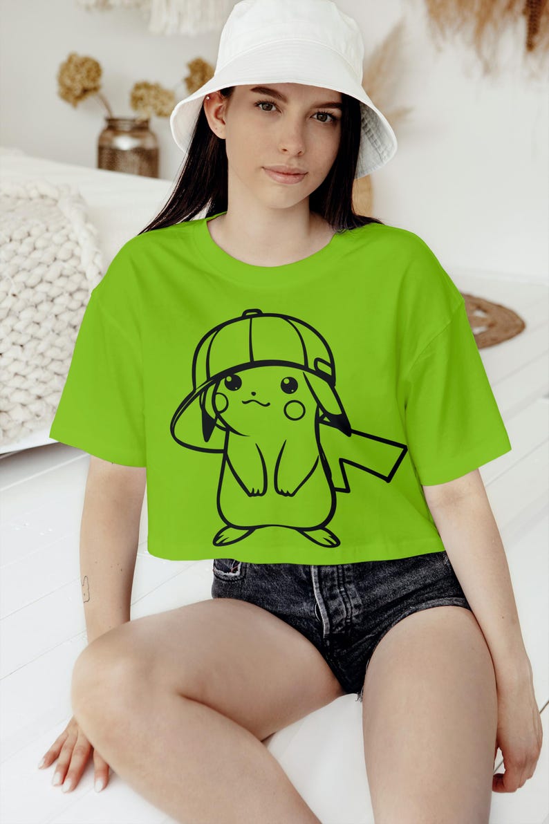 May include: A lime green crop top featuring a black outline illustration of a cartoon character wearing a cap. The person in the image is also wearing a white bucket hat and denim shorts.