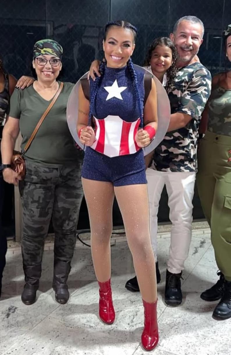 May include: A group of people posing for a photo. A person is wearing a Captain America-inspired costume with a blue top, shorts, and red boots. The costume includes a white star and a red and white chest piece. Other people are wearing camouflage and green outfits.