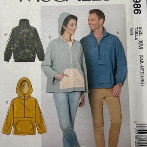 May include: McCall's sewing pattern M7986 featuring designs for hooded jackets and pullovers. The pattern includes options for a camouflage jacket, a gray hooded pullover with a peach pocket, and a mustard yellow hooded jacket.