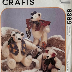 Può includere: Modello McCall's Crafts per realizzare tre orsi polari di peluche. Gli orsi sono bianchi con sciarpe, cappelli e accessori decorativi. Il numero del modello è 8389. Gli orsi sono posizionati su una superficie rocciosa e innevata.